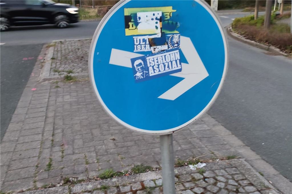Aufkleber auf einem Verkehrsschild, das auf einer Querungshilfe steht.