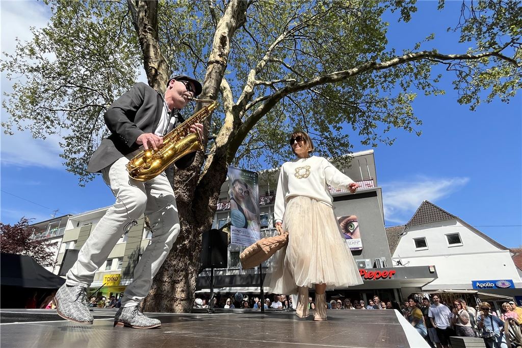 Frauen präsentieren bunte Mode auf dem Laufsteg. Ein Saxophonspieler spielt dabei.