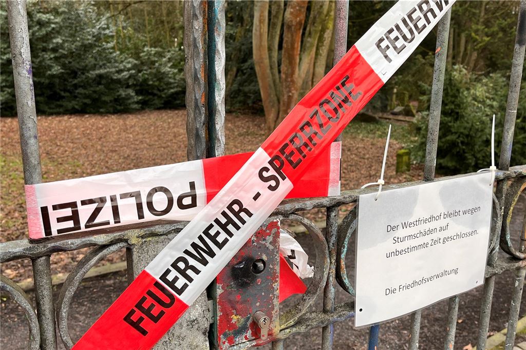 Sperrung nach Sturm: Stadt räumt Westfriedhof auf An einem Tor des Westfriedhofs in Unna hängt Flatterband der Feuerwehr und der Polizei neben einem Hinweisschild, das auf die Sperrung hinweist.