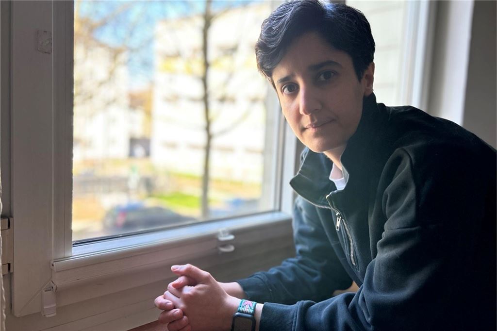 Kübra hat Long-Covid: „Man kann sein Leben verlieren, ohne zu sterben“ Kübra steht an einem Fenster, die Arme auf der Fensterbank abgestützt.