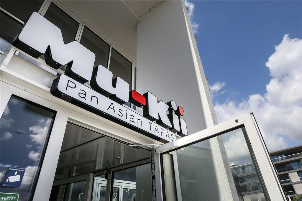 Essen retten im Süden Dortmunds: Übersicht der „Too Good To Go“ Lokale Die Aufnahme zeigt den Eingangsbereich des Restaurants "Mu-Kii Pan Asian Tapas". Über der Tür ist das beleuchtete Logo des Restaurants angebracht.