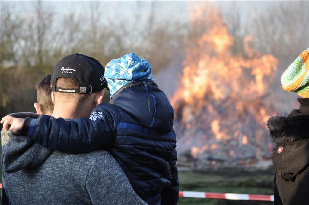 Dürfen Osterfeuer trotz Trockenheit stattfinden? Stadt Selm hat klare Tendenz Mann hat ein Kind auf dem Arm. Beide schauen sich ein großes Feuer an.