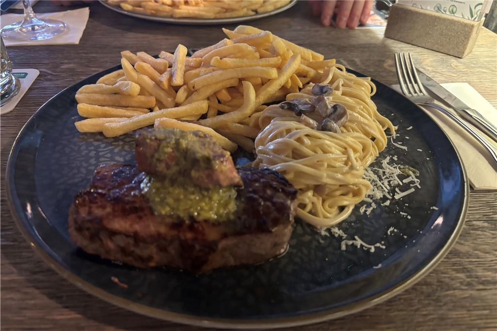 Steakrestaurant Wamo: Kann das All-you-can-Steak-Konzept überzeugen? Ein Teller mit einem Rumpsteak, Spaghetti aus dem Parmesanlaib und Pommes steht im Wamo in Dortmund auf einem Tisch.