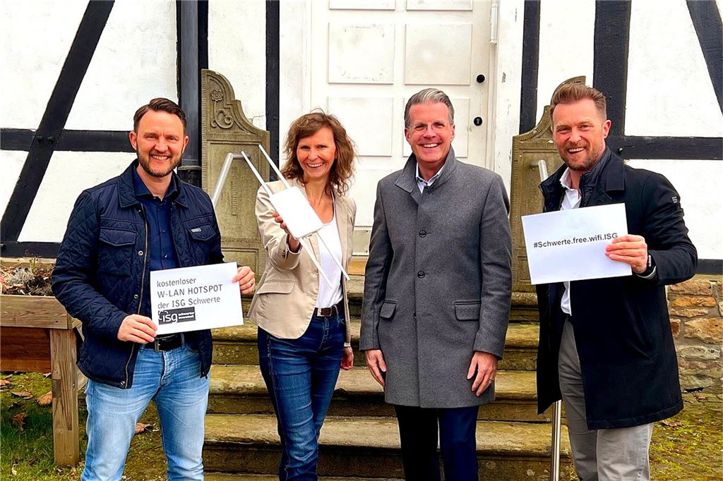 Öffentliches WLAN in City wächst: Wuckenhof und Bücherei angeschlossen Vier Personen vor einem Fachwerkhaus halten Plakate mit der Adresse eines öffentlichen WLAN-Netzes in der Hand.