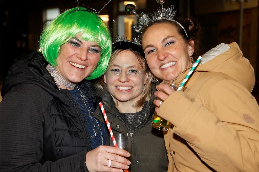 Eine Frau mit grüner Perücke und zwei weitere daneben lächeln in die Kamera.