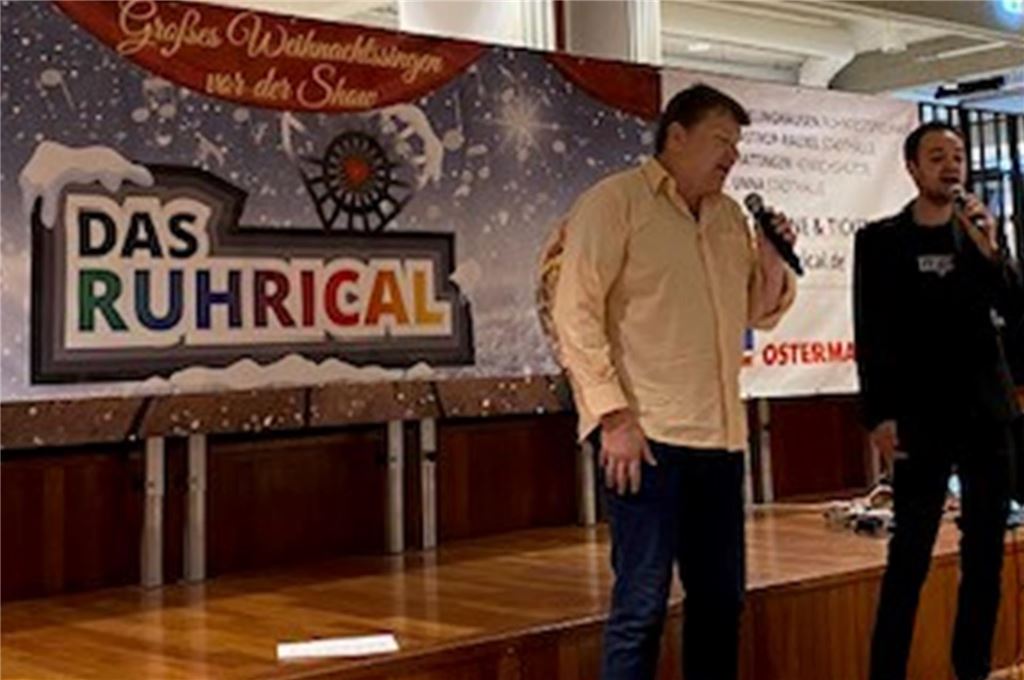 Großes Weihnachtssingen vor Ruhrical-Show im Dezember Bernd Böhne (links) und Robin Lindemann proben einen Song für die Aufführung des Ruhricals. Sie stehen auf der Bühne vor einem Plakat des Ruhricals und halten Mikrofone in den Händen.