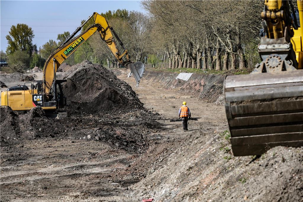 Riesen-Baustelle am Hafen: Boden für neues ICE-Werk wird bereitet Ein Bauarbeiter geht zwischen Baufahrzeugen über das Aushub-Gelände.