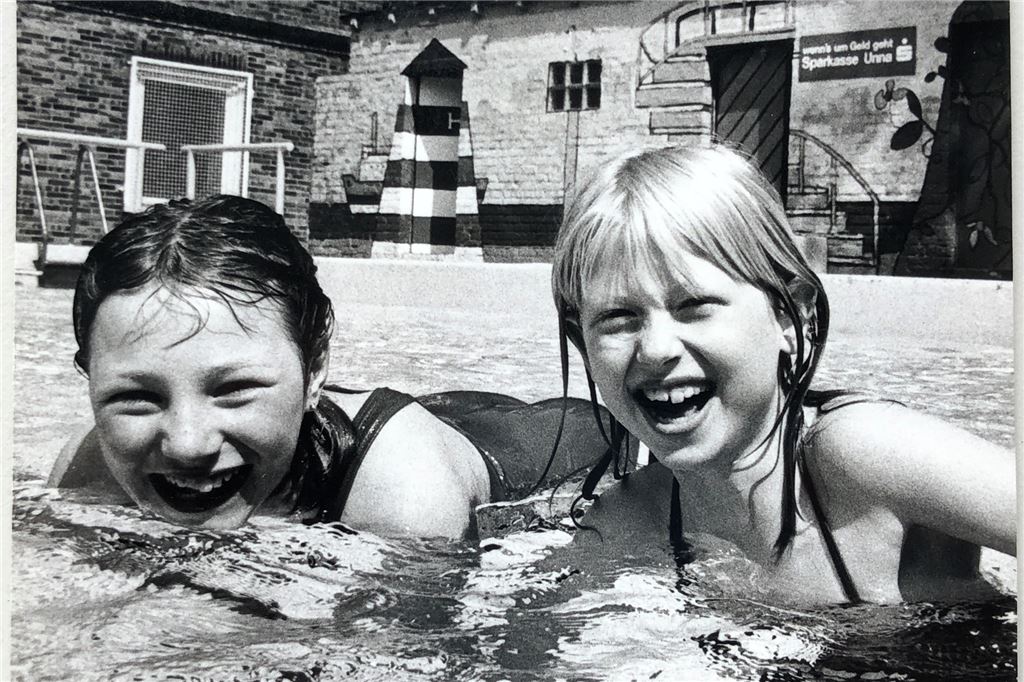 Die Freibadretterin der ersten Stunde kann gar nicht schwimmen Darum geht es: Kinder haben Spaß im Wasser. Im Hintergrund ist die Mauer der Umkleiden zu sehen – bemalt von Künstler Wolfgang Buhre.