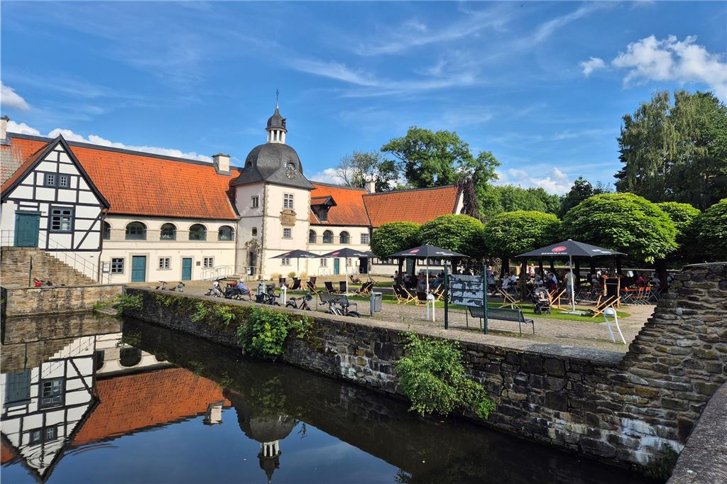 Traditionelle Biergärten im Dortmunder Süden: Alle Infos im Überblick Das Wasserschloss, umgeben von einem Wassergraben, spiegelt sich im ruhigen Wasser wider, während Besucher den Biergarten im Freien genießen.
