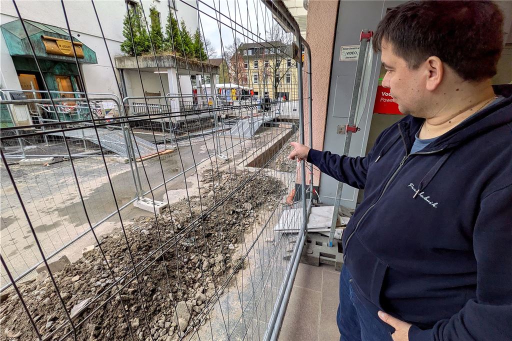 Bauzaun sperrt Weg zum City-Center: „Kunden laufen rum wie Pik Sieben“ Ein Kaufmann zeigt auf eine Baustelle vor seinem Geschäft.