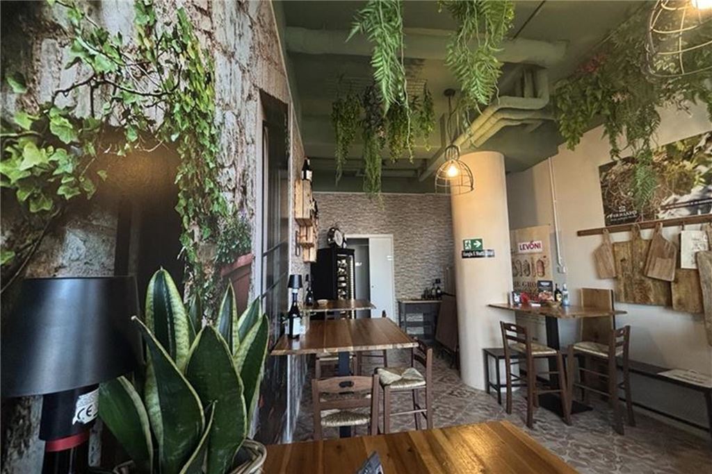 Bistro von „La Mortadella“ im Restaurant-Check Innenansicht eines Restaurants mit Tischen und Stühlen. Die Wände sind mit Pflanzenmustern verziert und von der Decke hängen Hängepflanzen.