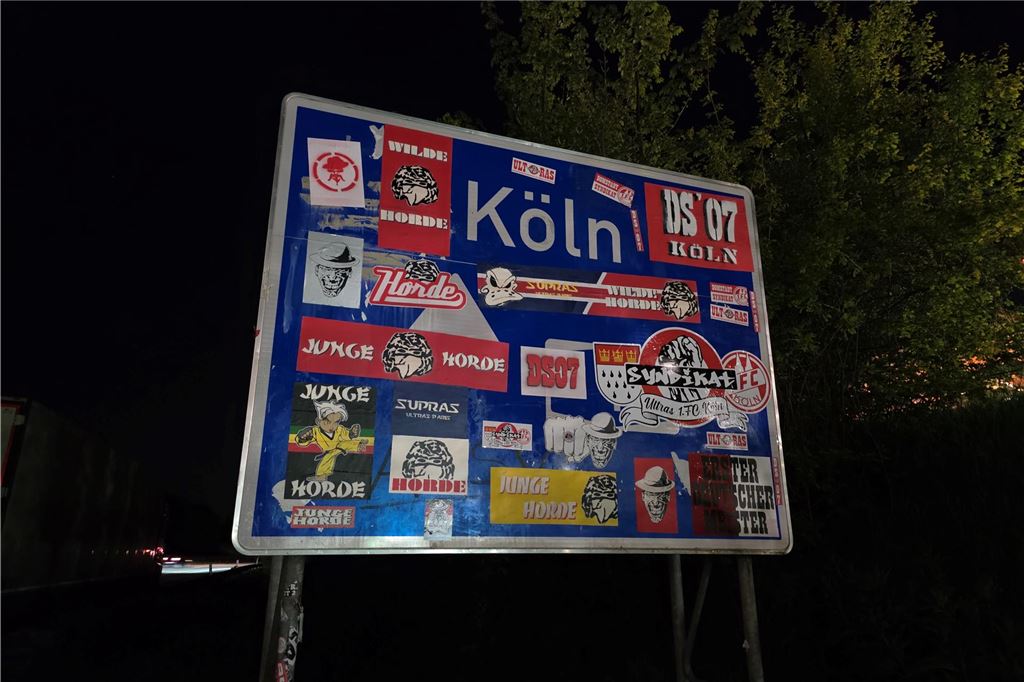 Fußballfans lösen Polizeieinsatz an Rastplatz aus: Viele Polizei am Abend vor Ort Ein Verkehrsschild auf der Autobahn ist mit vielen Stickern beklebt. Nur das Wort Wort "Köln" ist noch lesbar