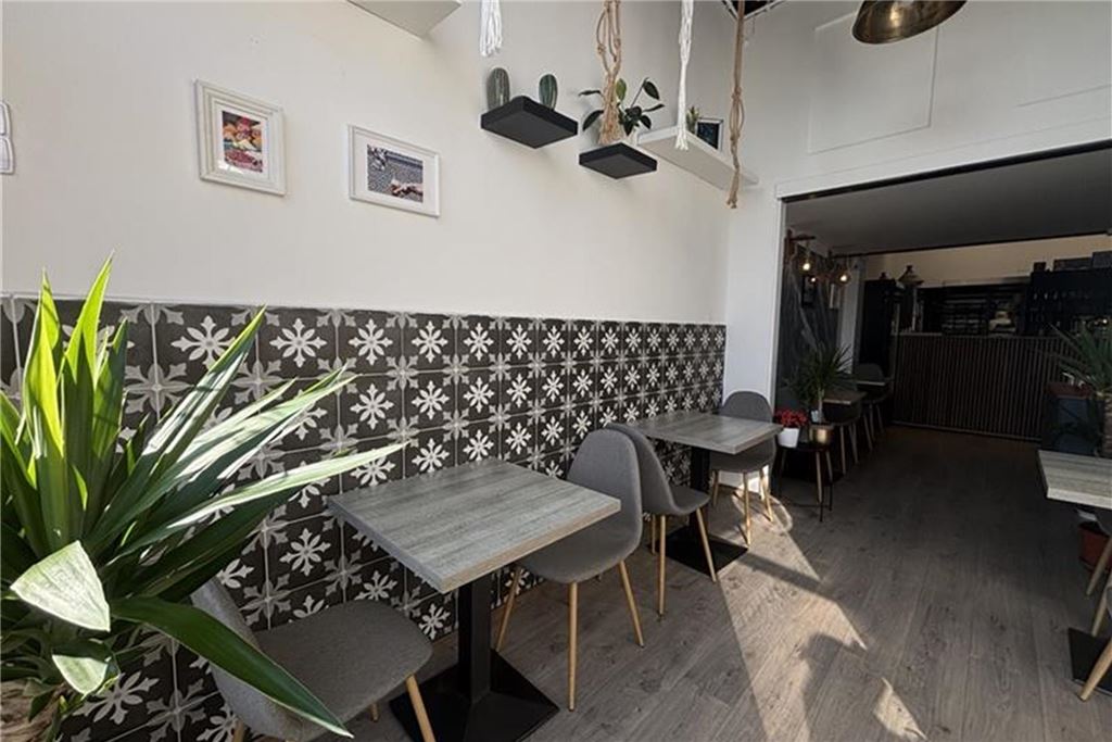 Restaurant-Check: Bei „Amlounge“ kann man den ganzen Tag frühstücken Innenansicht eines Cafés mit Tischen und Stühlen. Die Einrichtung umfasst Fliesen mit Blumenmuster, Pflanzen und dekorative Regale an den Wänden.
