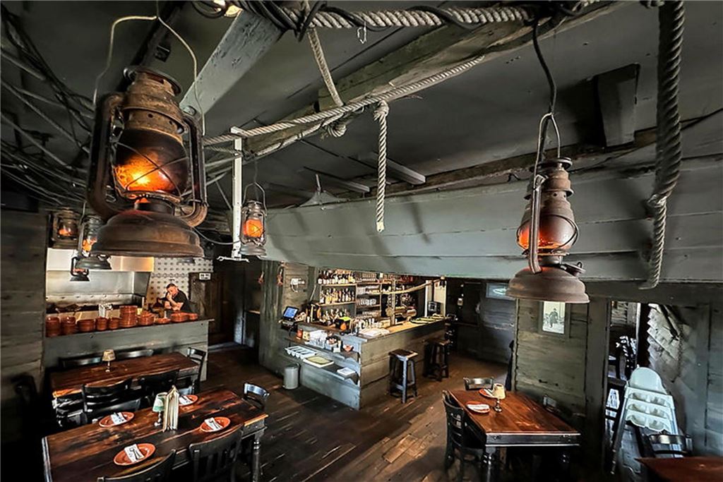 „O Mira“ im Restaurant-Check: Was kann der „Carlos“-Nachfolger? Innenansicht eines Restaurants mit rustikaler Einrichtung. Mehrere Holztische sind mit Gedecken versehen und werden durch kleine Lampen beleuchtet.