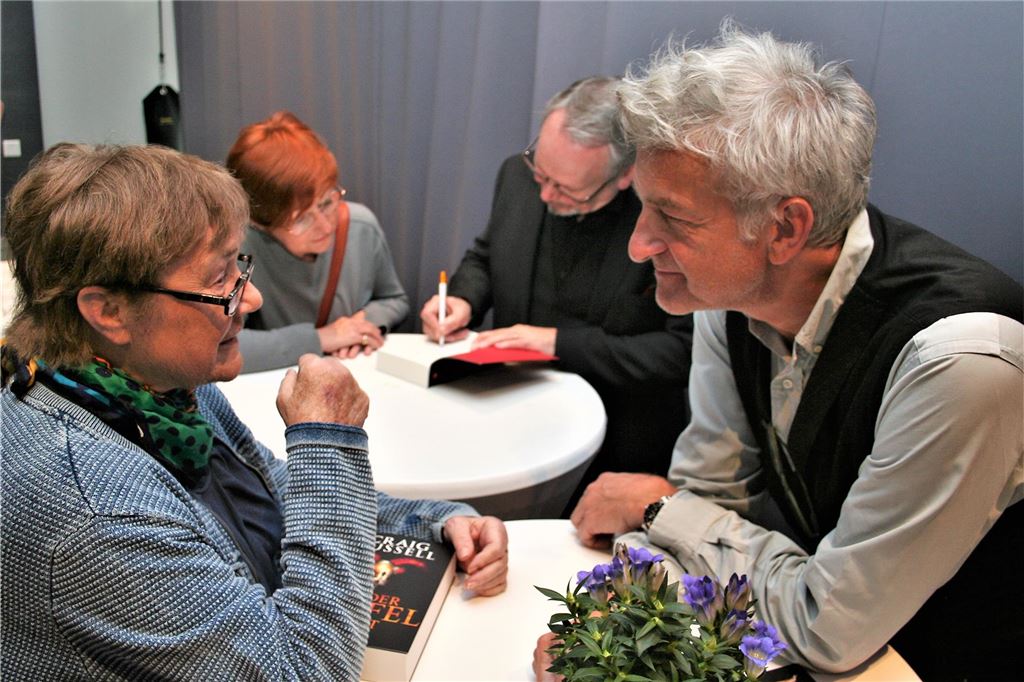 Isabell Archan schreibt den Fröndenberg-Krimi 2024 für Mord am Hellweg Ein Mann und eine Frau unterhalten sich, während im Hintergrund ein Buch signiert wird.
