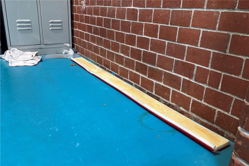 Beschwerde über Müll, Schmutz und lose Teile in Turnhalle In einer Turnhalle liegen Müll und ein Brett in einer Ecke