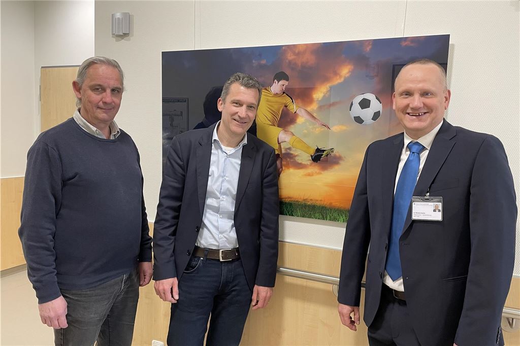 Neuer Chefarzt in Kirchlinde ist Top-Mediziner auf Focus-Bestenliste Dr. Holger Böhm, Pflegedirektor Axel Westermann und Professor Dr. Sebastian Seitz, der neue Chefarzt der Orthopädie am Katholischen Krankenhaus Dortmund-West, stehen vor einem Fußball-Bild, das auf der Deluxe-Station hängt.