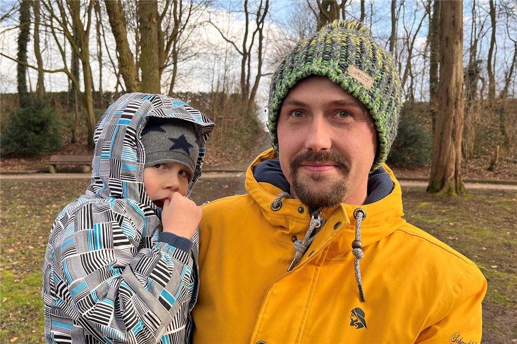 Tüten-Appell, damit Hundekot nicht Mensch und Natur gefährdet Ein Mann mit Wollmütze und gelber Jacke in einem Park trägt ein Kind auf dem Arm