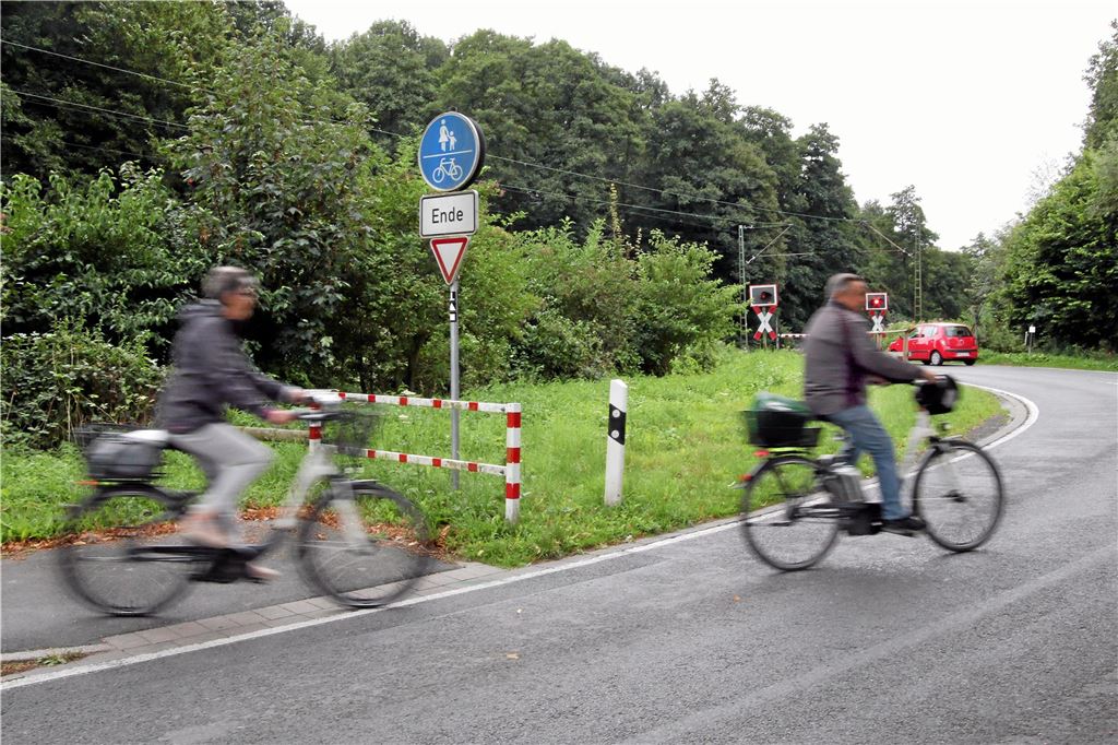 Radfahrer in Mühlhausen haben endlich ihren eigenen Bahnübergang Zwei Radfahrer fahre von einem Radweg auf eine Straße. Im Hintergrund steht ein Auto vor einem geschlossenen Bahnübergang