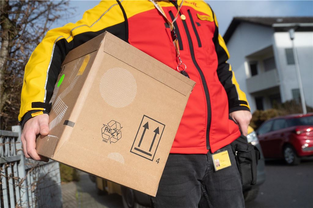 Paket verschwindet spurlos: DHL weist jede Schuld von sich Ein DHL-Zusteller trägt ein mittelgroßes Paket unter seinem Arm.