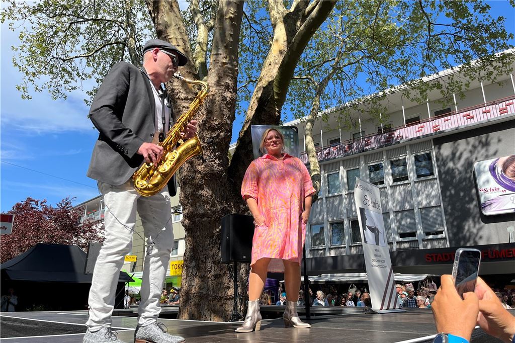 Frauen präsentieren bunte Mode auf dem Laufsteg. Ein Saxophonspieler spielt dabei.