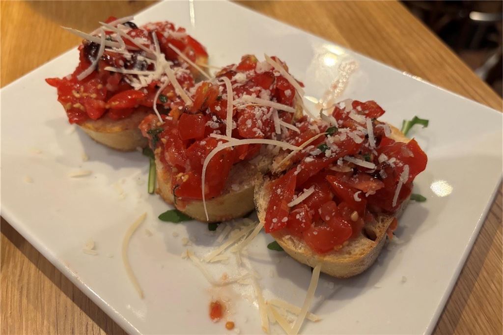 Pasadena im Restaurant-Check: Italienischen Küche mit Kneipen-Flair Drei Ciabatta-Scheiben belegt mit Tomaten, Basilikum und geriebenem Käse werden auf einem weißen Teller als Bruschetta serviert.