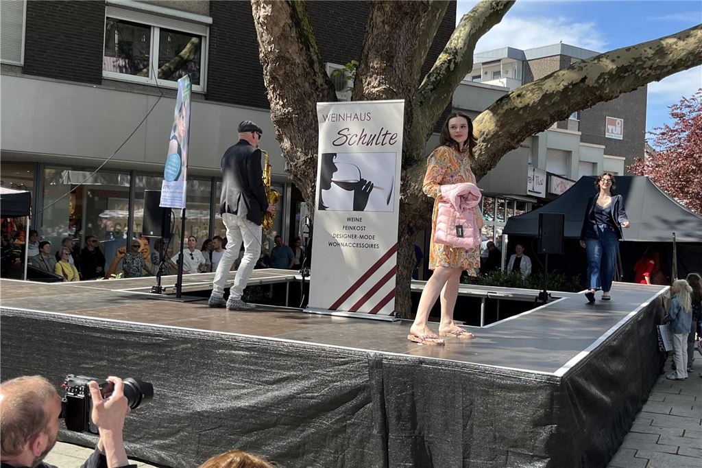 Frauen präsentieren bunte Mode auf dem Laufsteg. Ein Saxophonspieler spielt dabei.
