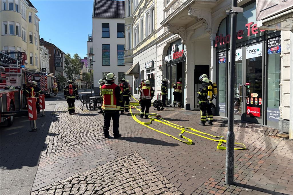 Feuerwehreinsatz in der Innenstadt von Unna: Pizzaofen in Imbiss fängt Feuer Ein Feuerwehrauto im Anschnitt sowie zwei Feuerwehrleute stehen vor dem Imbiss Multi Kebap in der Bahnhofstraße in Unna