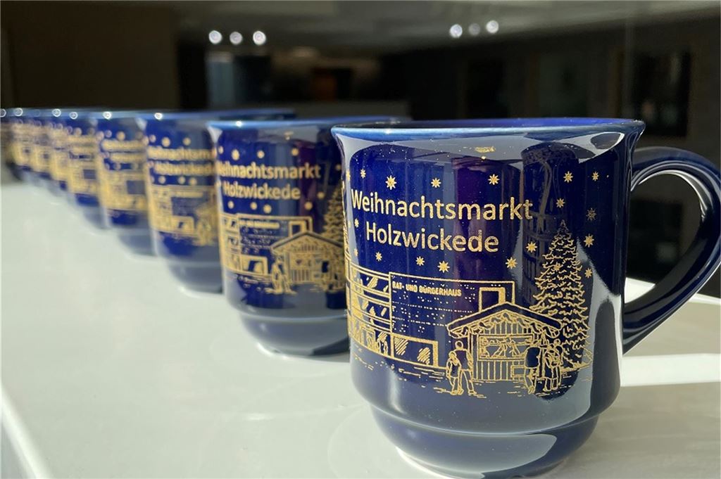 3000 neutrale Tassen für den Weihnachtsmarkt Auf einem Brett stehen mehrere blaue Tassen mit der Aufschrift "Weihnachtsmarkt Holzwickede".
