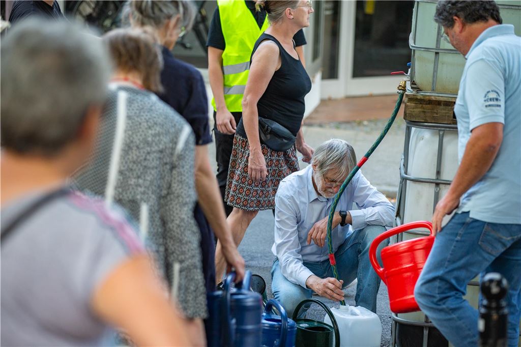 Christian Gramsch hält 245 Jungbäume am Leben Bei einer Gießaktion 2023 in Unna befüllen Menschen Gießkannen und Kanister mit Wasser aus einem Tank.