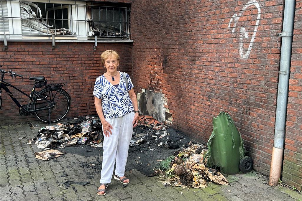 Wieder brennen Container: Brandserie geht weiter Hausbewohnerin Edith Brix vor den Resten der verbrannten Mülltonnen. Bei der Brandstiftung im August an der Kämerstraße in Kamen wurden die Hauswand und ein Auto beschädigt.