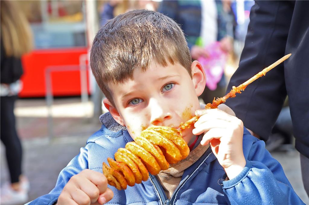 Ein Junge beißt in einen Spieß mit Kartoffelscheiben. 