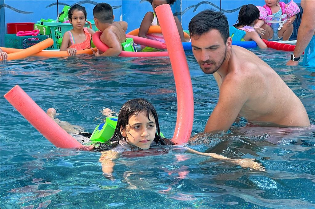 270 Kinder lernen im Bornekamp, sich über Wasser zu halten Im Bornekamp-Freibad in Unna schwimmt ein Kind mit Schwimmhilfen und Unterstützung eines Schwimmlehrers durch das Becken.
