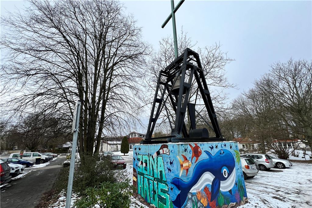 Finanzielle Schieflage: Unnaer Kirche will Gemeindezentrum verkaufen Auf einem Block mit dem Schriftzug "Jona-Haus", mit Meereshintergrund, steht eine Glocke mit Kreuz.