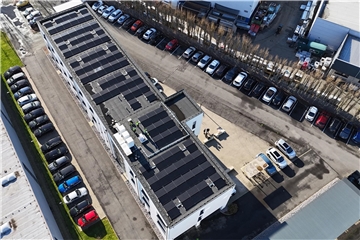 Ein gewerbliches Gebäude mit Photovoltaikanlagen auf dem Dach. Darum herum parken Autos.