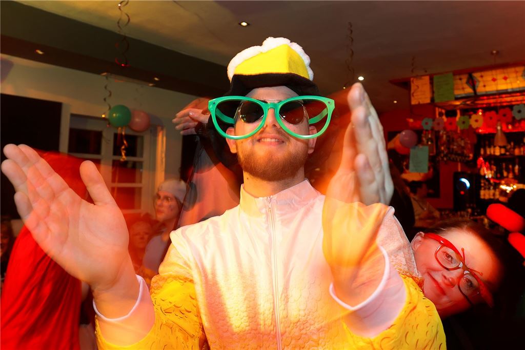 Ein Mann in gelber Kleidung mit großer, grüner Brille klatscht.