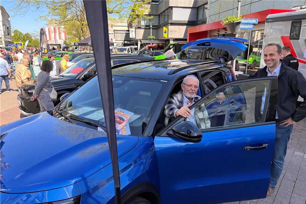 Bilder von der Mobilitätsschau am verkaufsoffenen Wochenende: Da ist für alle was dabei! In einem blauen Auto sitzt ein Mann, ein anderer lehnt an der geöffneten Tür