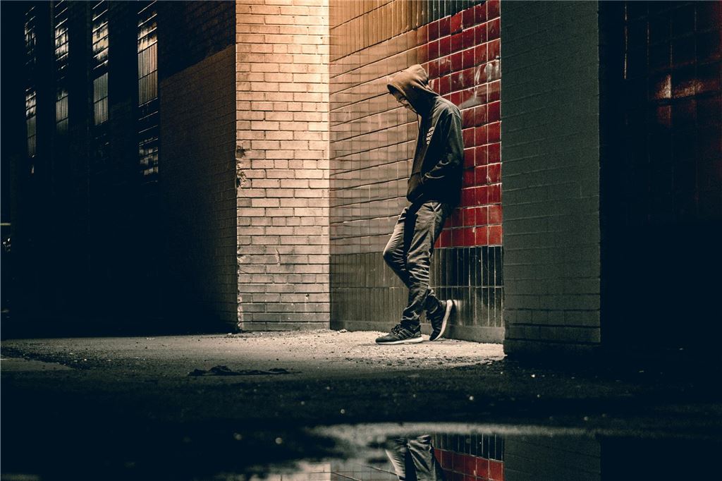 Klaas (35) ist kokainabhängig: „Meine Sucht ist ein Beziehungskiller“ Ein junger Mann steht nachts mit der Kapuze ins Gesicht gezogen an einer Wand gelehnt.