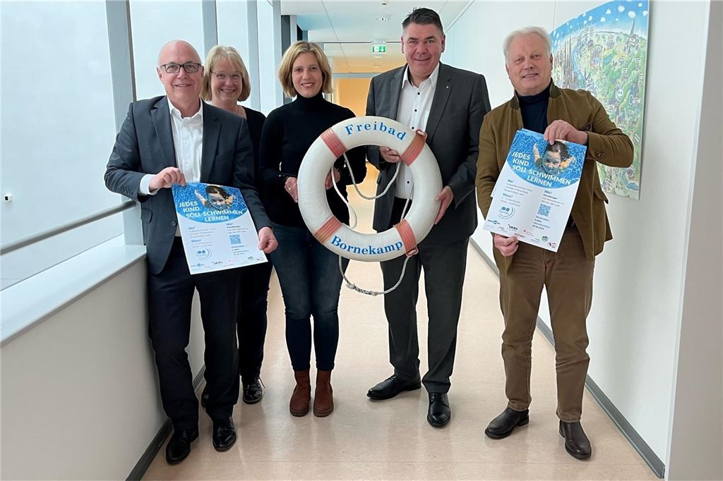 „Auf Förderungen angewiesen“: Freibad Dellwig hofft auf Unterstützung von Landrat Löhr Matthias Fischer von der UKBS, Organisatorin Katja Sträde, Sandra Ruiz, Geschäftsführerin Bündnis für Familie, Landrat Mario Löhr und Klaus Stindt vom KSB Unna (v.l.) stehen in einem Flur und halten Plakate hoch.