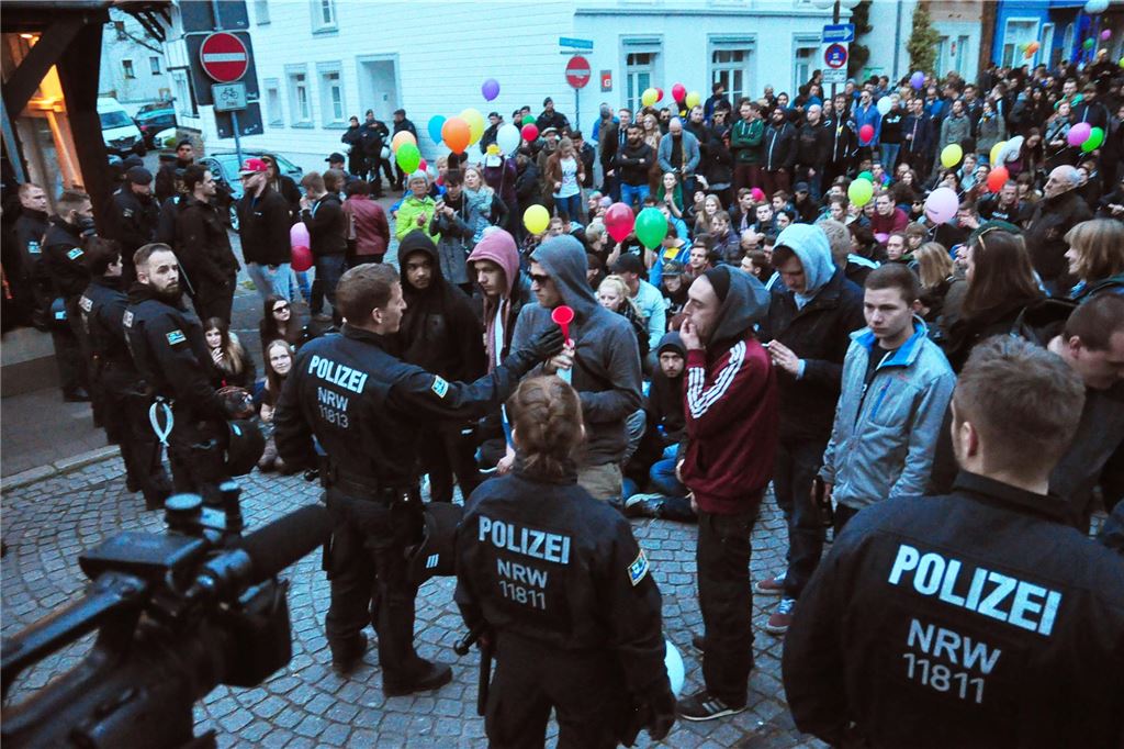 Gegendemos wollen AfD in Unna „nicht kommentarlos“ lassen Während einer Demo in Unna im Jahr 2026 stehen oder sitzen zahlreiche Demonstranten einer Reihe von Polizisten gegenüber