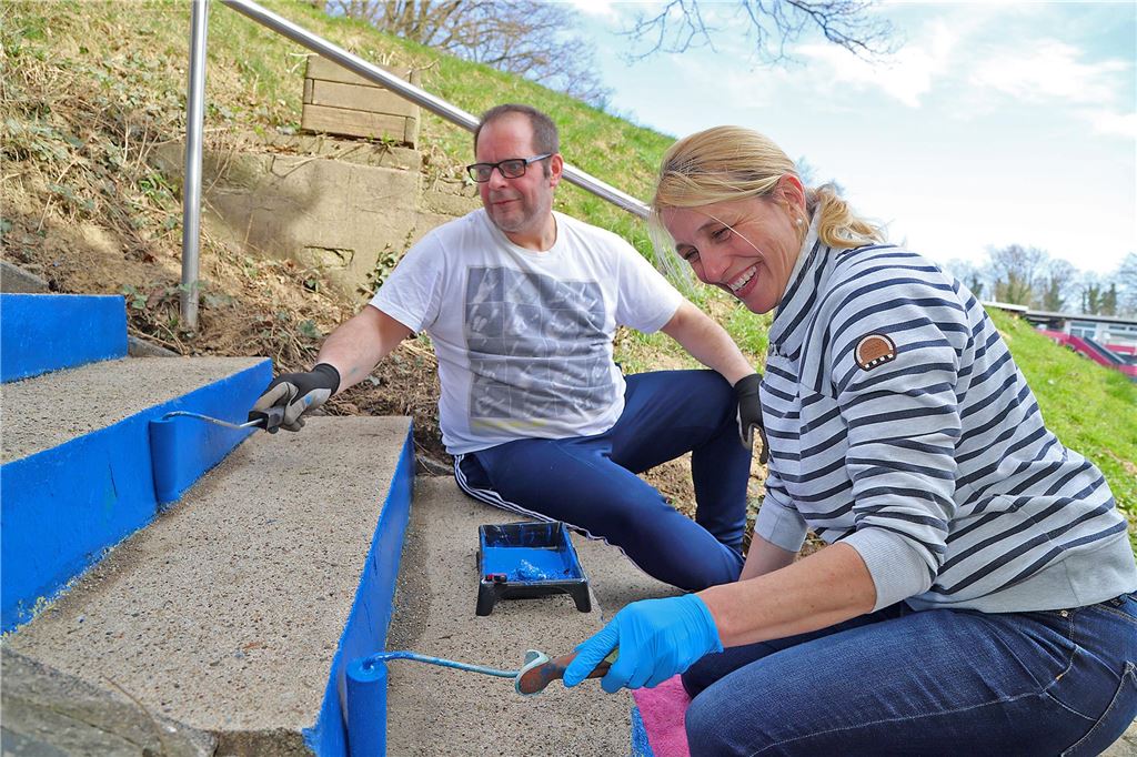 Matthias Schmoll und Verena Krebber-Hortmann streichen Treppenstufen in blauer Farbe. 