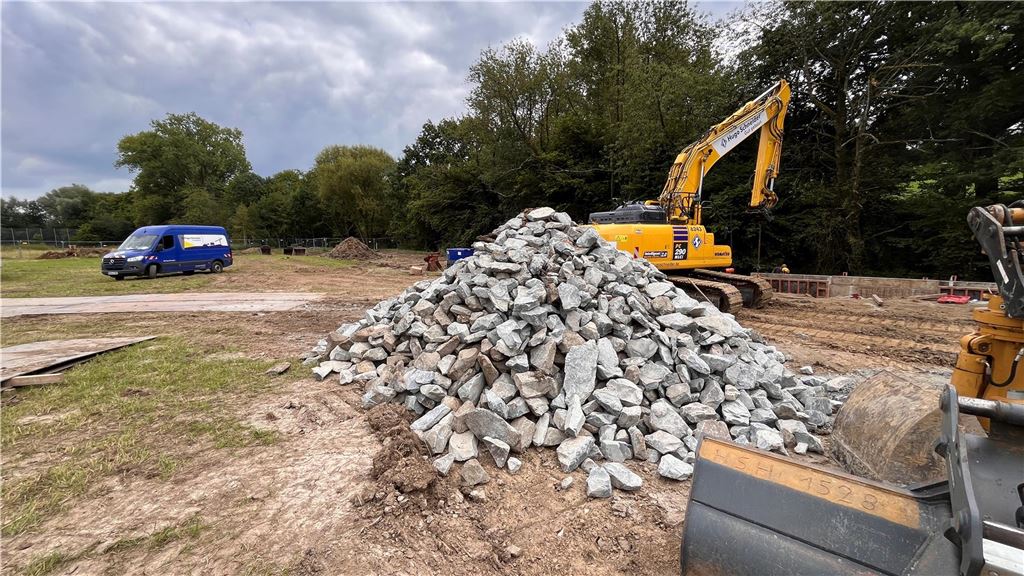 Naturschutz ist Pflicht: Stadtbetriebe bauen Staufläche in Billmerich Auf einer Baustelle in Unna-Billmerich liegt ein Haufen Wasserbausteine. Dahinter stehen ein Bagger und ein Lieferwagen.