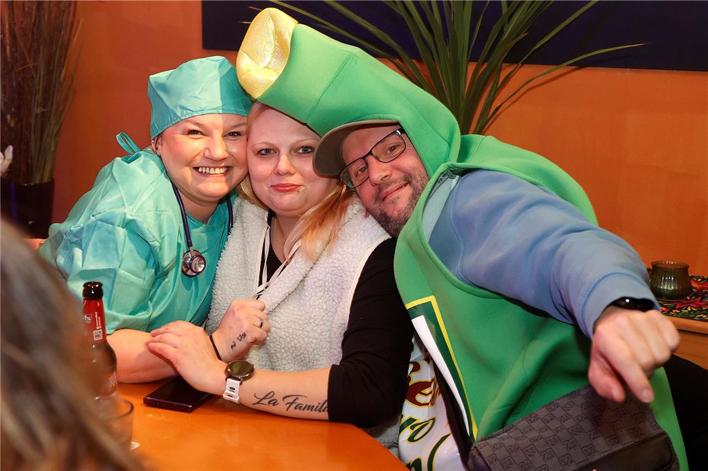 Eine "Krankenschwester", eine Bierflasche und eine weitere Frau sitzen am Tisch. 