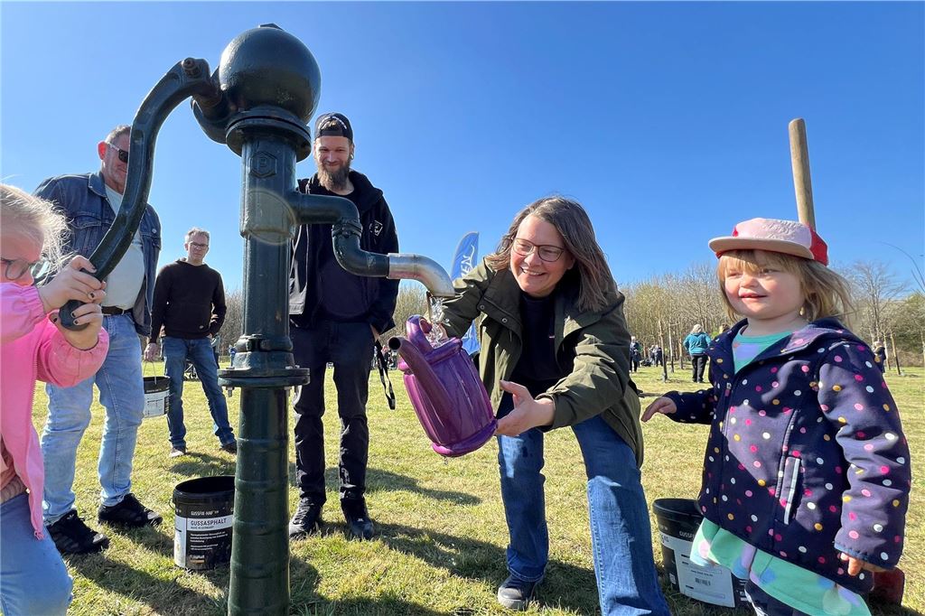 Pflanzfest an der Overberger Straße: Jubiläumswald wächst weiter Mehrere Erwachsene und zwei kleine Mädchen stehen an einer Wasserpumpe und füllen eine lilafarbene Gießkanne.