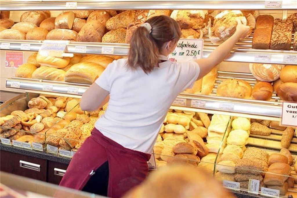 Diese Bäcker öffnen am 1. Mai: Hier gibt’s frische Brötchen Eine Verkäuferin holt in einer Bäckerei ein Brot aus einer Auslage.