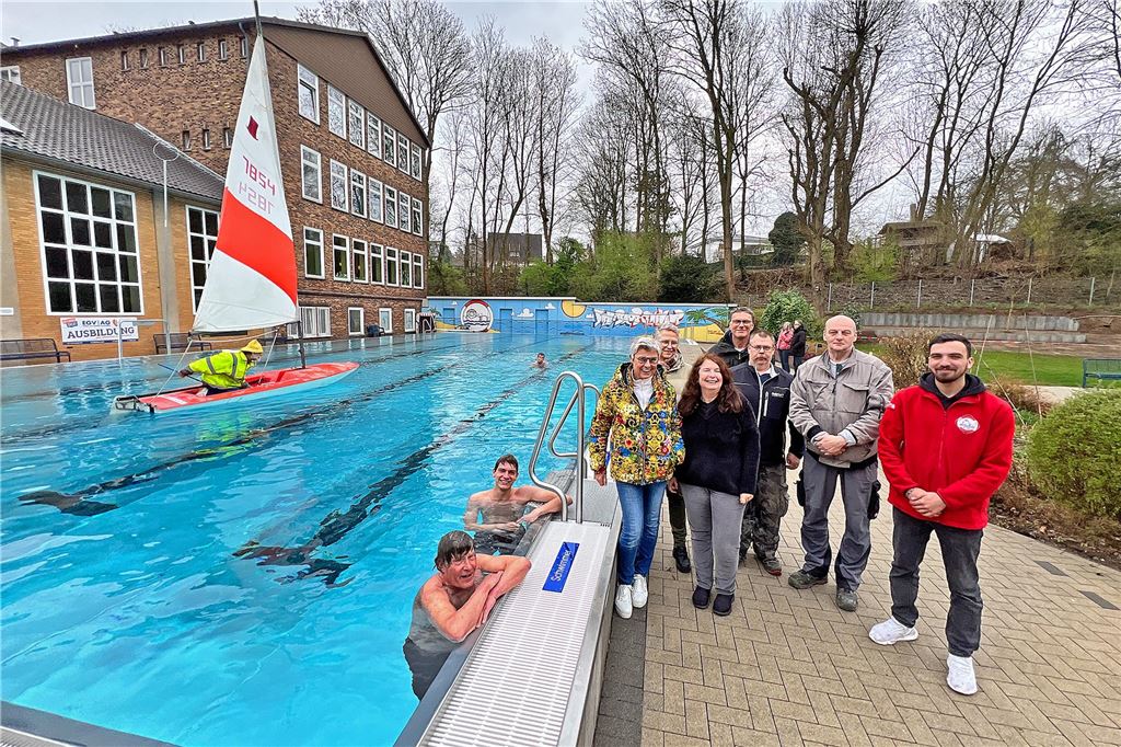 Mitglieder des Freibadvereins Bornekamp in Unna stehen neben dem Schwimmbecken, in dem Ende März schon zwei Schwimmer im Wasser sind.