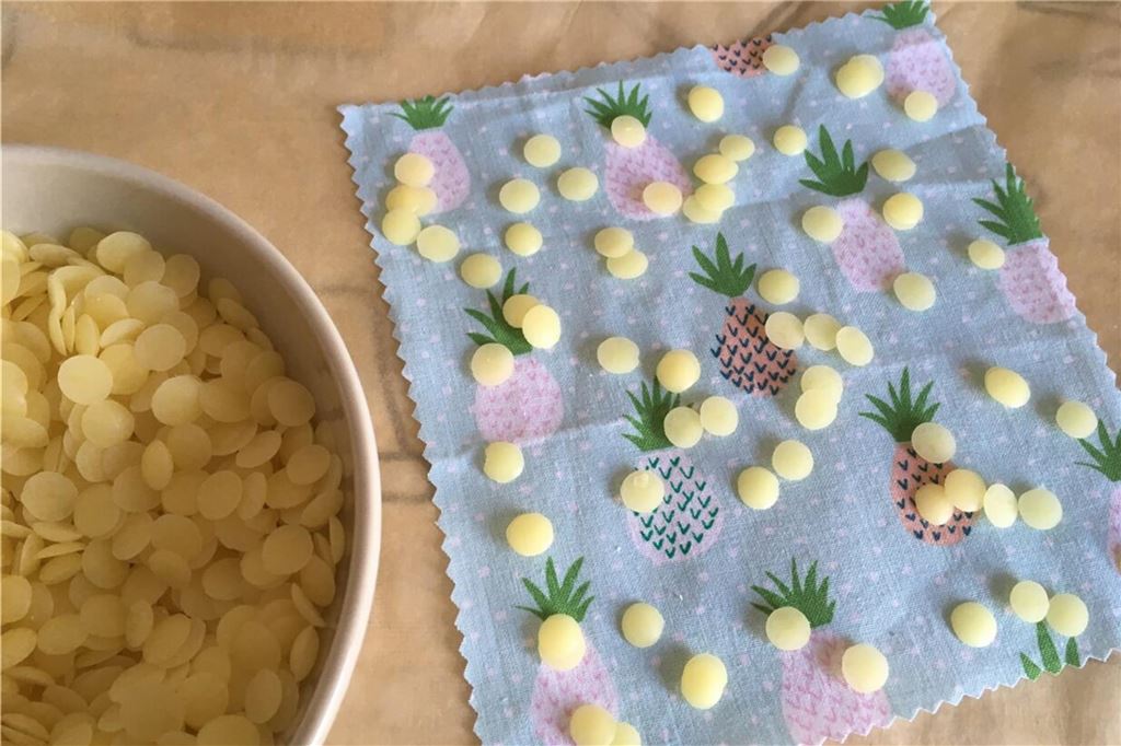 So macht man Bienenwachstücher selbst: Einfache Anleitung zum Nachbasteln Wachstropfen und ein buntes Stück Stoff liegen auf einem Tisch.