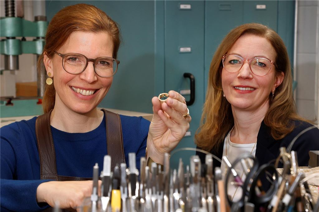 Stephanie Telgmann (l.) und Dorothée Telgmann in der Werkstatt der gleichnamigen Goldschmiede in Kamen. Sie lächeln in die Kamera. Eine der Schwestern hält einen Ring hoch.