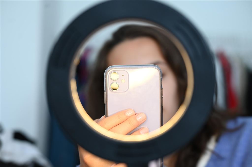 Depressionen oder ADHS bei TikTok: „Internet ersetzt keine Diagnostik“ Eine junge Frau ist durch ein aufgebautes Ringlicht zu sehen, sie hält ein Smartphone in der Hand.