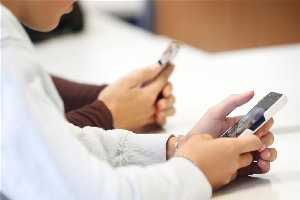 Umgang mit Handyverbot: Gesamtschule legt innovatives Konzept vor Zwei Schülerinnen schauen im Klassenraum auf ihr Handy.